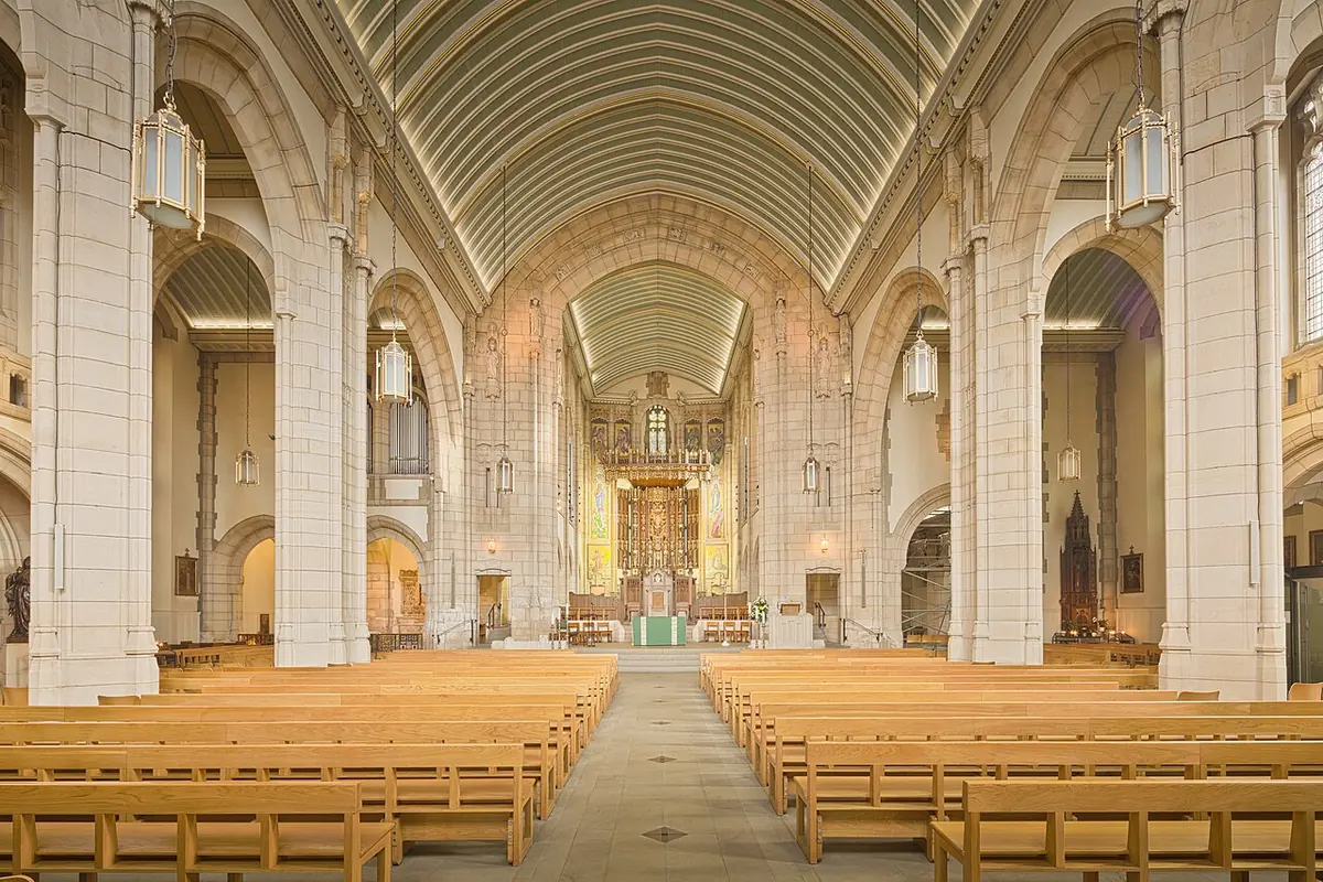 The pale stone nave of Leeds Cathedral with rows of wooden pews leading up to the high altar and sanctuary