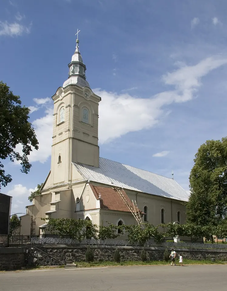 A white church with a tall bell tower and a red roof on a sunny day in the village of Bilky in Transcarpathia