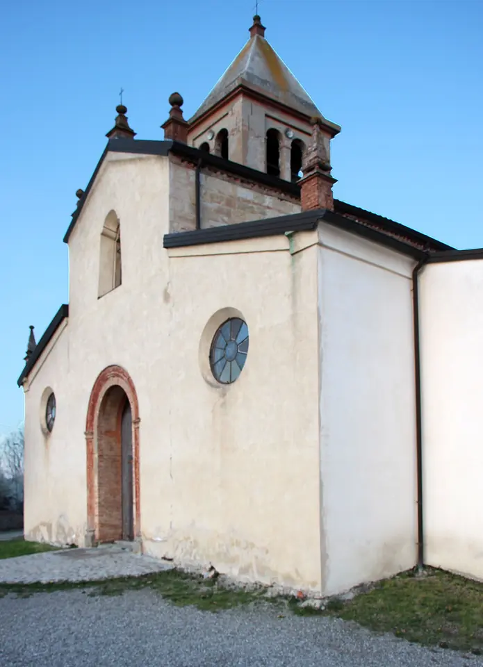 The cream-colored front of a small country church with a round window, an arched brick doorway and a bell tower behind