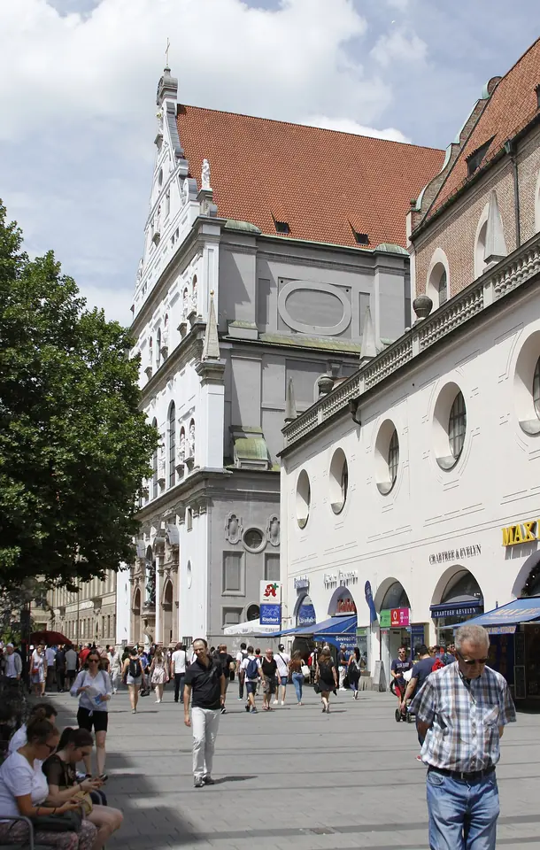 Tall white Renaissance church facade with a stepped gable and statues in niches, on a busy pedestrian street with shoppers