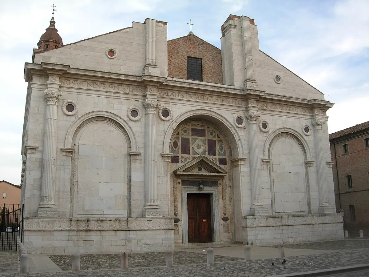 The white marble Renaissance front of Rimini Cathedral, with three great arches, a pediment over the door and a brick upper wall