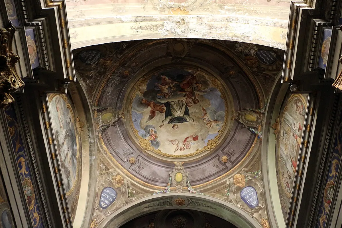A painted ceiling vault with a round fresco of a Dominican friar carried up to heaven by angels, framed by gilded stucco