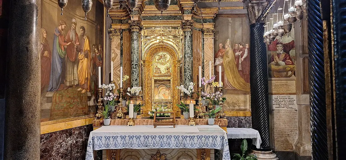 The gilded and marble chapel of Our Lady of Good Counsel in the shrine at Genazzano, with candles and flowers on the altar and frescoes on either side
