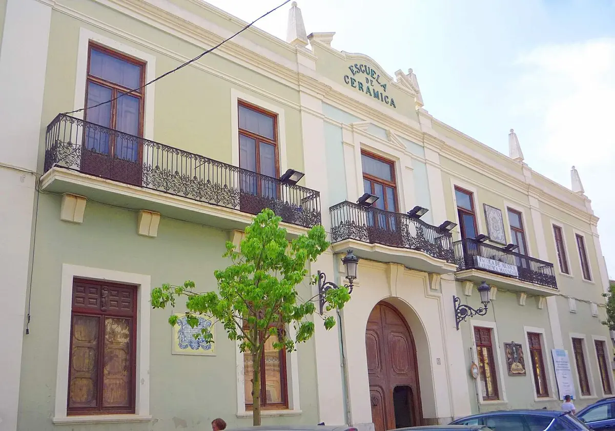 The pale green two-story front of the ceramics school of Manises, with iron balconies, an arched wooden door and a tiled sign above the roofline
