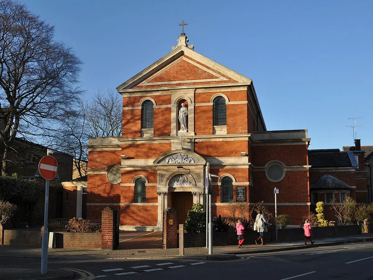 A red-brick Catholic church with a classical white-trimmed front, a statue in a niche above the door, and bare trees on a street corner