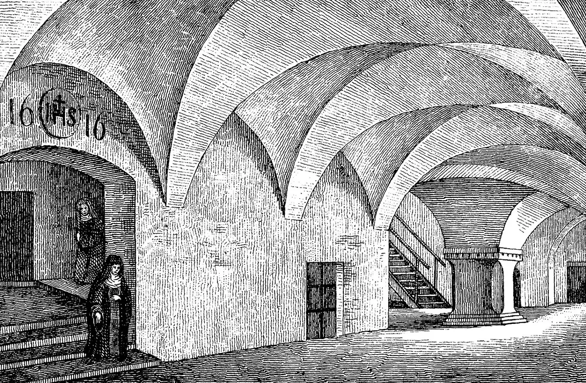 Old engraving of a long vaulted convent corridor with heavy doors, a staircase and a nun in a dark habit standing near a doorway