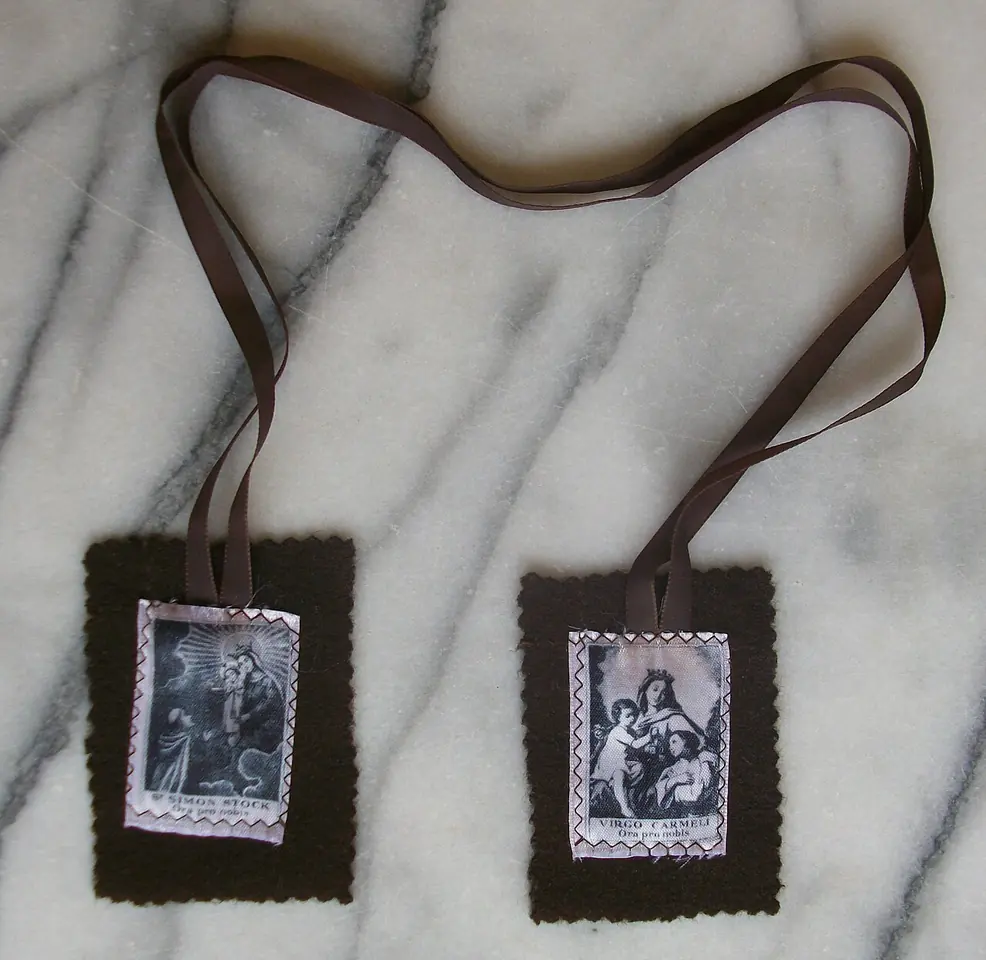 Two rectangles of dark brown felt on brown ribbons, each with a small printed holy picture, lying on white marble