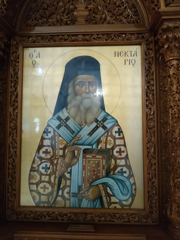 Icon of St. Nektarios in a carved wooden frame, an old bishop in a blue veil and patterned vestments, blessing and holding a book against a gold background