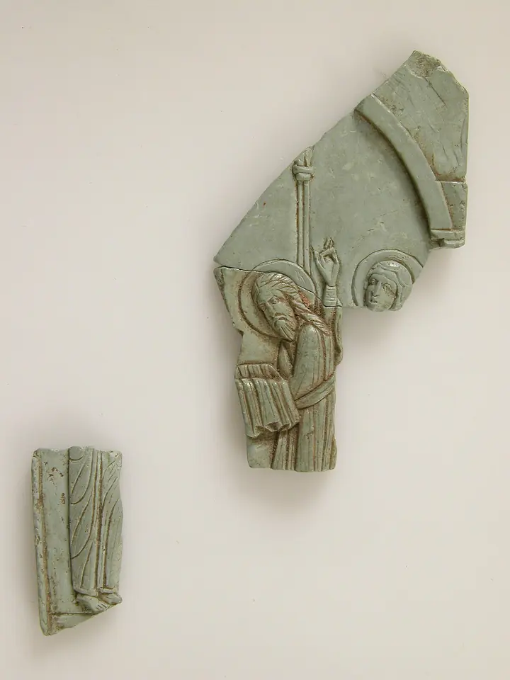 Two pale green carved stone fragments of a Byzantine icon, the larger showing a bending figure under an arch reaching forward with veiled hands