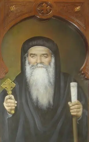 Portrait of an elderly bishop with a long white beard, wearing a black monastic hood with small crosses, holding a gold hand cross and a staff