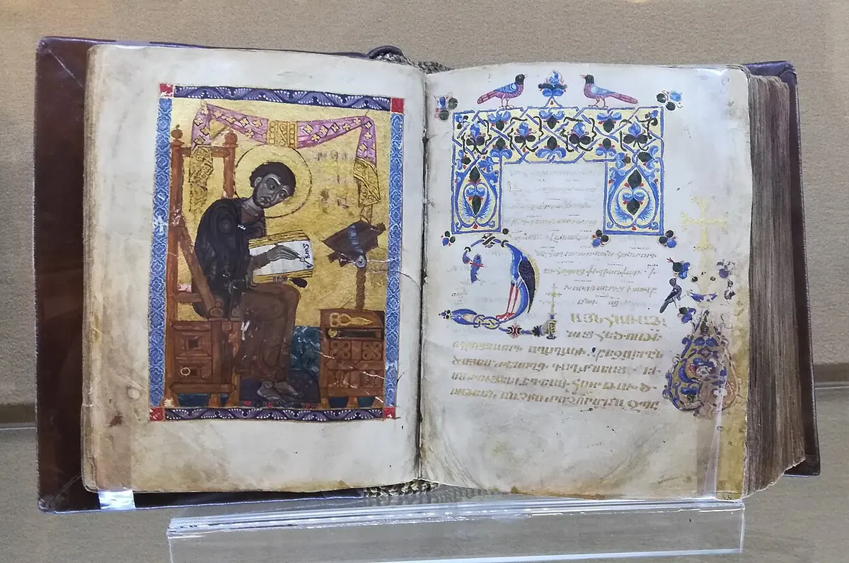Open medieval Armenian manuscript with a portrait of a monk writing at a desk on the left page and an ornamented title page on the right