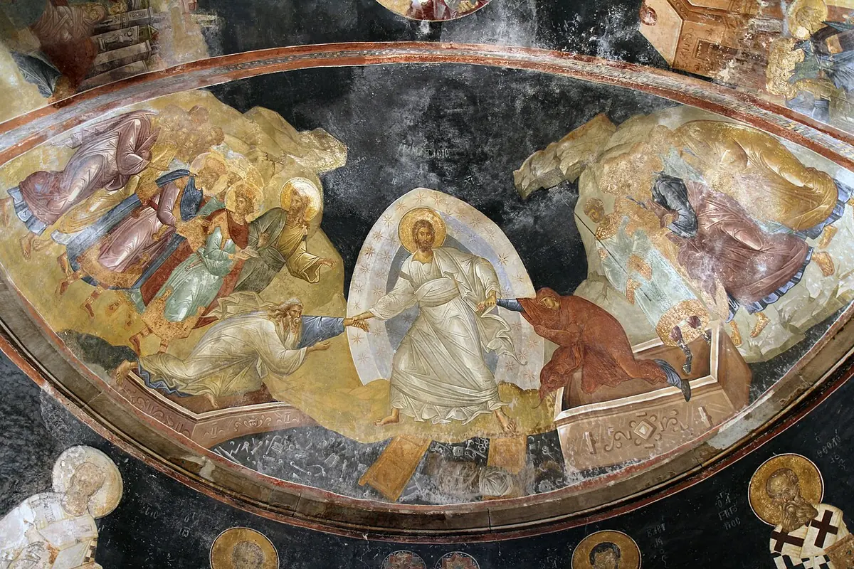 Byzantine fresco in a half-dome showing Christ in white robes standing on the broken gates of hell, pulling Adam and Eve up out of their tombs by the wrists