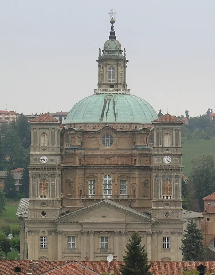 The great oval green dome and towers of the Sanctuary of Vicoforte seen above rooftops and trees in Piedmont