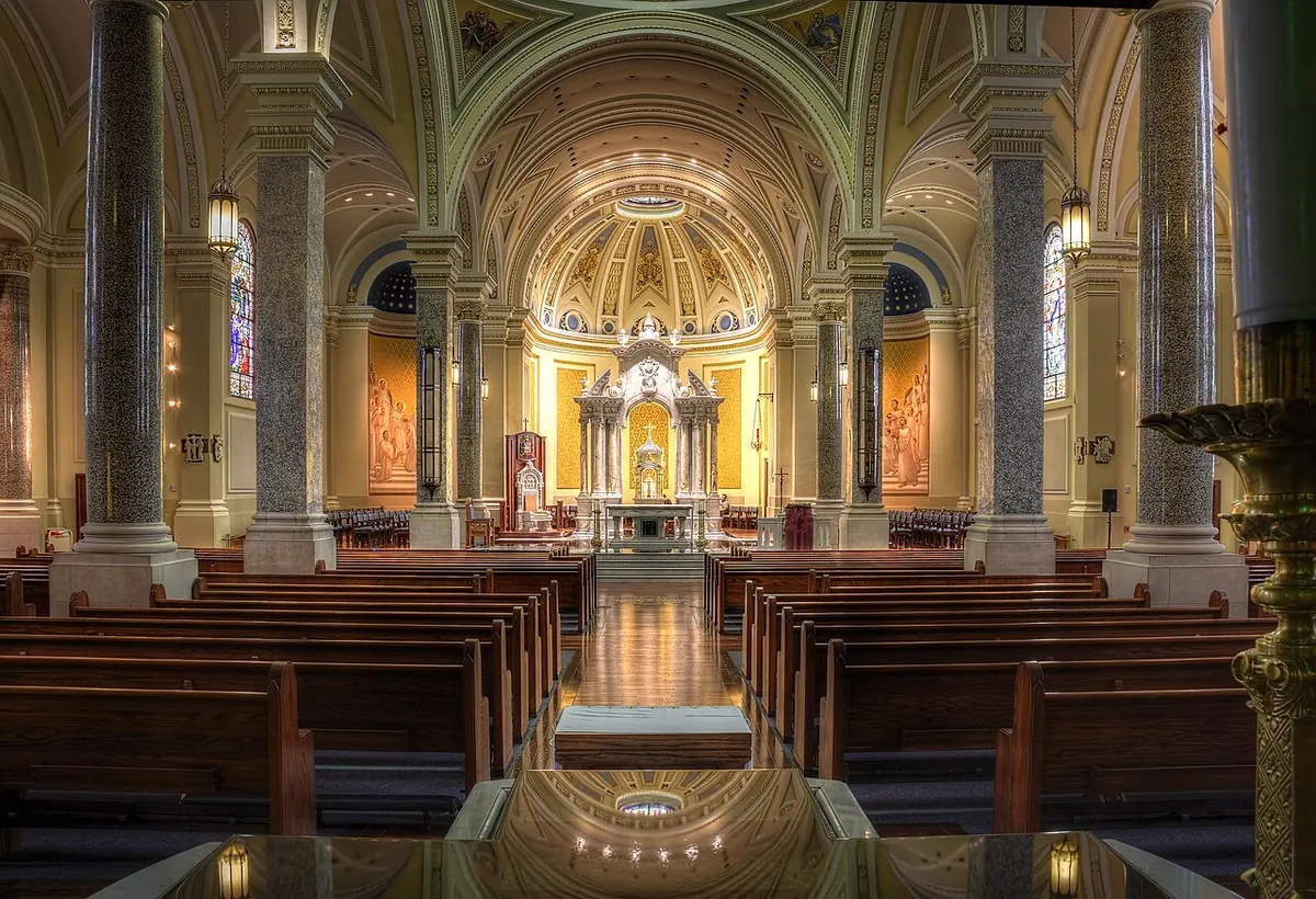 Wide view down the nave of a cathedral with marble columns, a coffered gold ceiling and a high altar under a dome