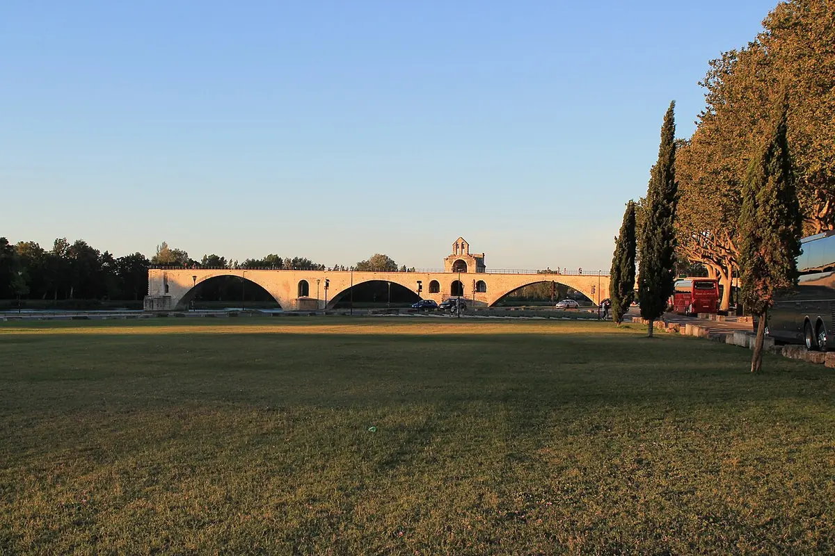 The surviving stone arches of the medieval bridge of Avignon with its small chapel, seen across a lawn at sunset