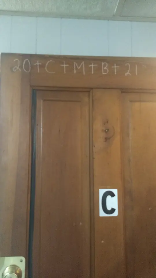 Wooden apartment door with 20+C+M+B+21 written in white chalk across the top of the frame