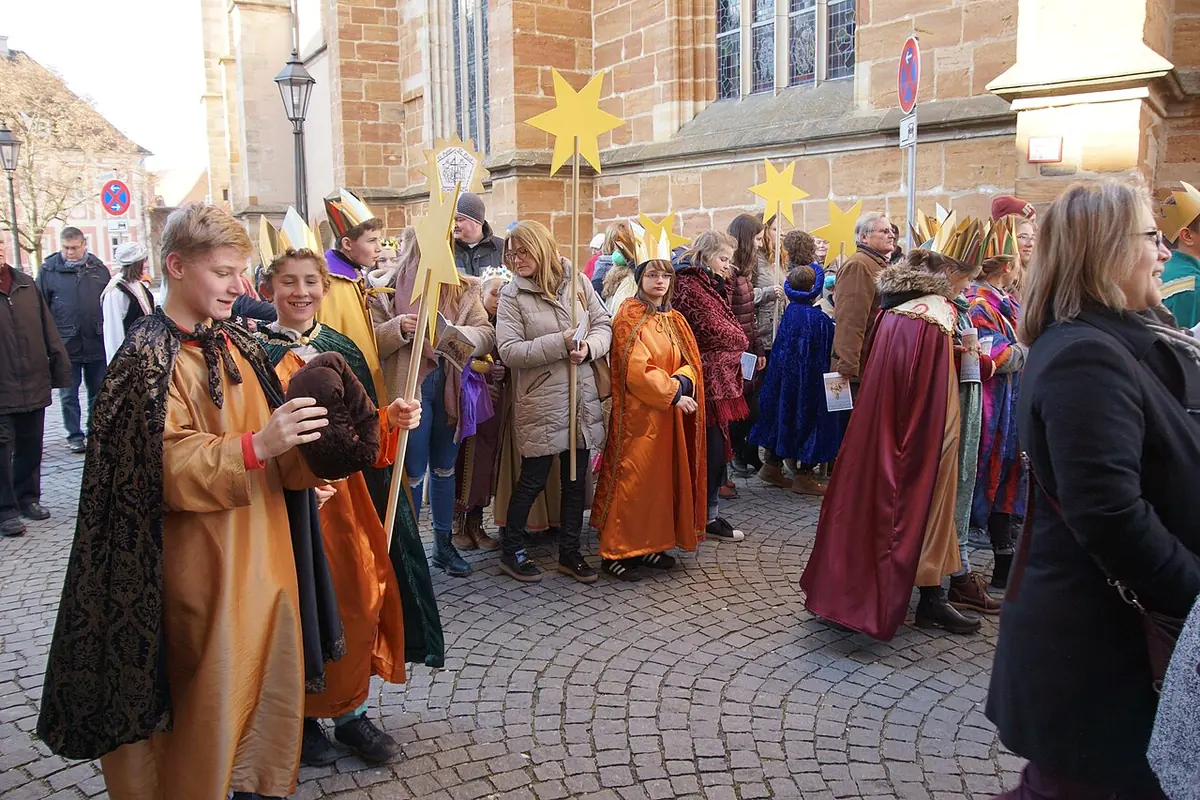 Crowd of children dressed as the three kings in colorful robes and paper crowns, carrying golden stars on poles through a town square