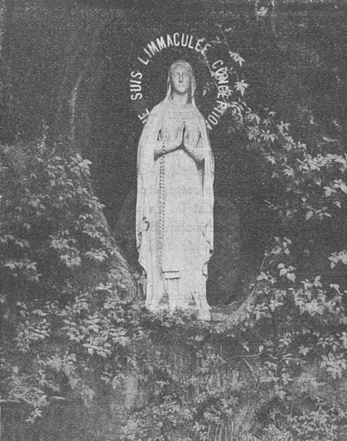 Fotografía antigua de la estatua blanca de la Virgen de Lourdes en su nicho de roca, rodeada de hiedra, con la inscripción Je suis l'Immaculée Conception en lo alto