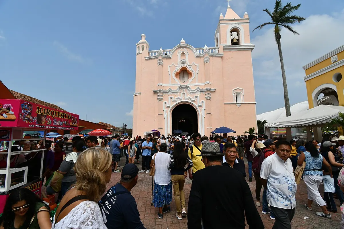 Una multitud de fieles y visitantes camina hacia la fachada rosa y blanca del santuario de la Candelaria de Tlacotalpan, entre puestos de feria y palmeras
