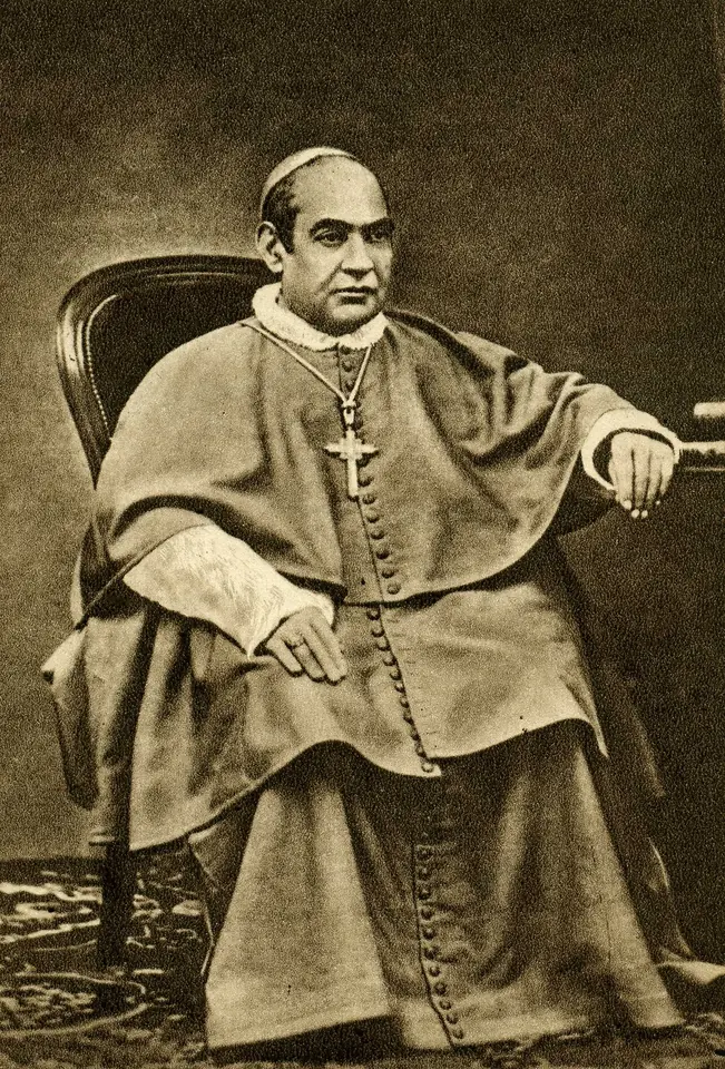 Fotografía antigua en sepia de un arzobispo robusto, de rostro serio, sentado en un sillón, con sotana, muceta y una cruz pectoral
