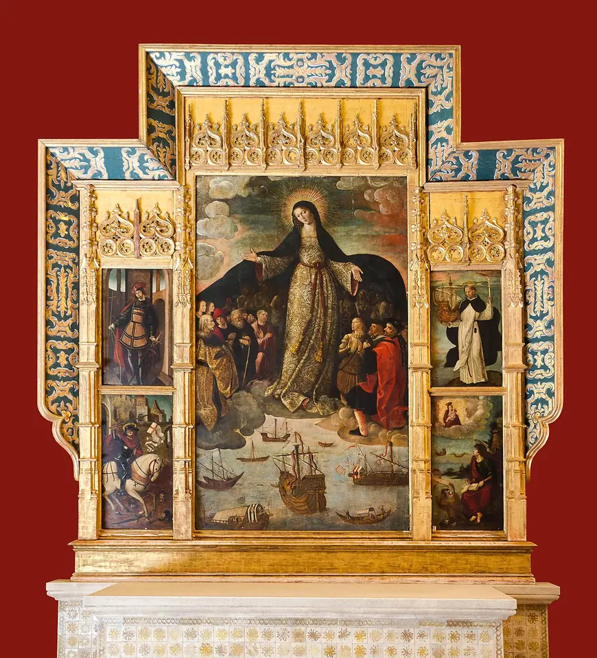 Retablo dorado de cuya tabla central la Virgen María, en el cielo, abre su manto oscuro sobre navegantes y caballeros arrodillados, con naves y carabelas en el mar a sus pies, entre tablas laterales con santos