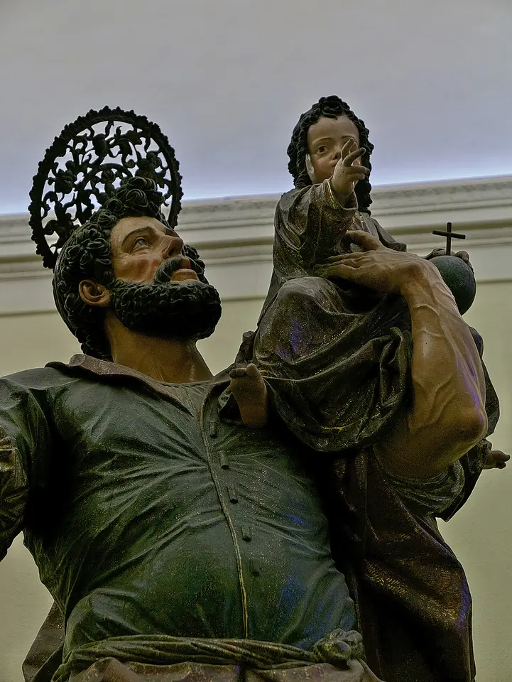 Detalle de una talla de madera policromada de San Cristóbal barbado, con aureola de rayos, que alza la vista hacia el Niño Jesús sentado sobre su hombro con el globo de la cruz