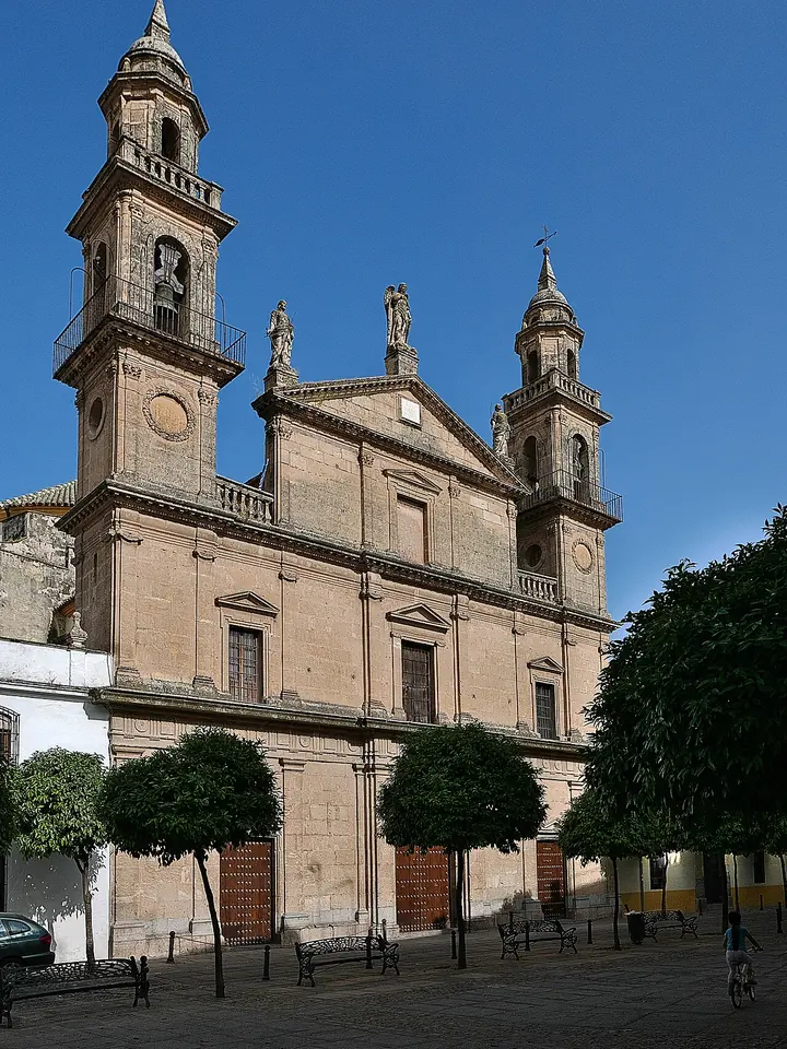 Fachada neoclásica de piedra dorada de la iglesia del Juramento de San Rafael en Córdoba, con dos torres de campanario y estatuas sobre el frontón, bajo un cielo azul intenso