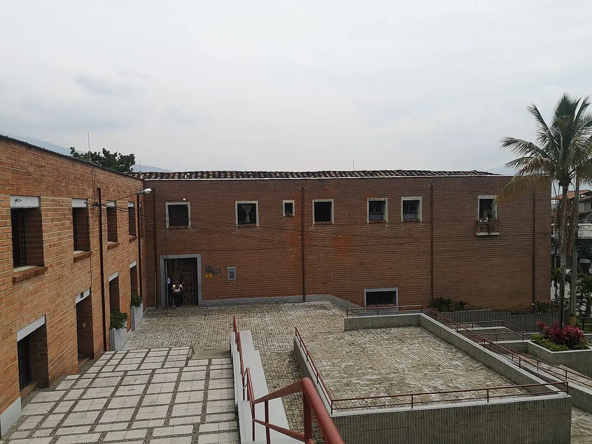 El edificio de ladrillo del Museo Etnográfico Madre Laura en Medellín, con un patio de baldosas y barandas, y palmeras al fondo