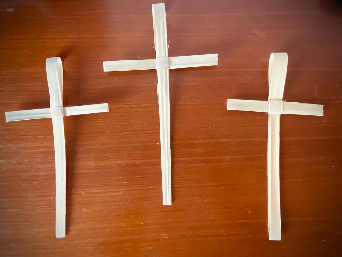 Tres crucecitas dobladas con tiras de hoja de palma seca, sobre una mesa de madera
