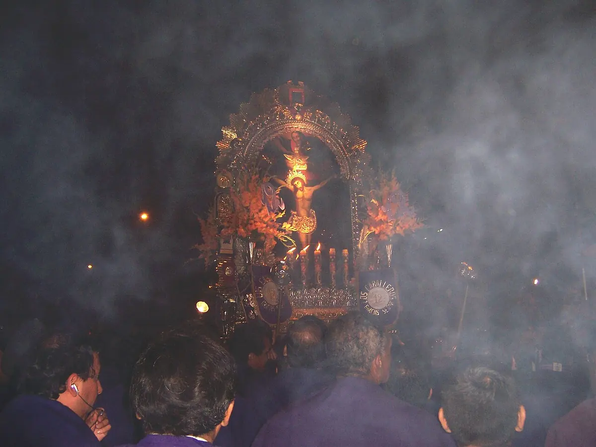 Las andas de plata del Señor de los Milagros iluminadas con velas, de noche, entre una nube de incienso y la multitud de devotos con hábito morado