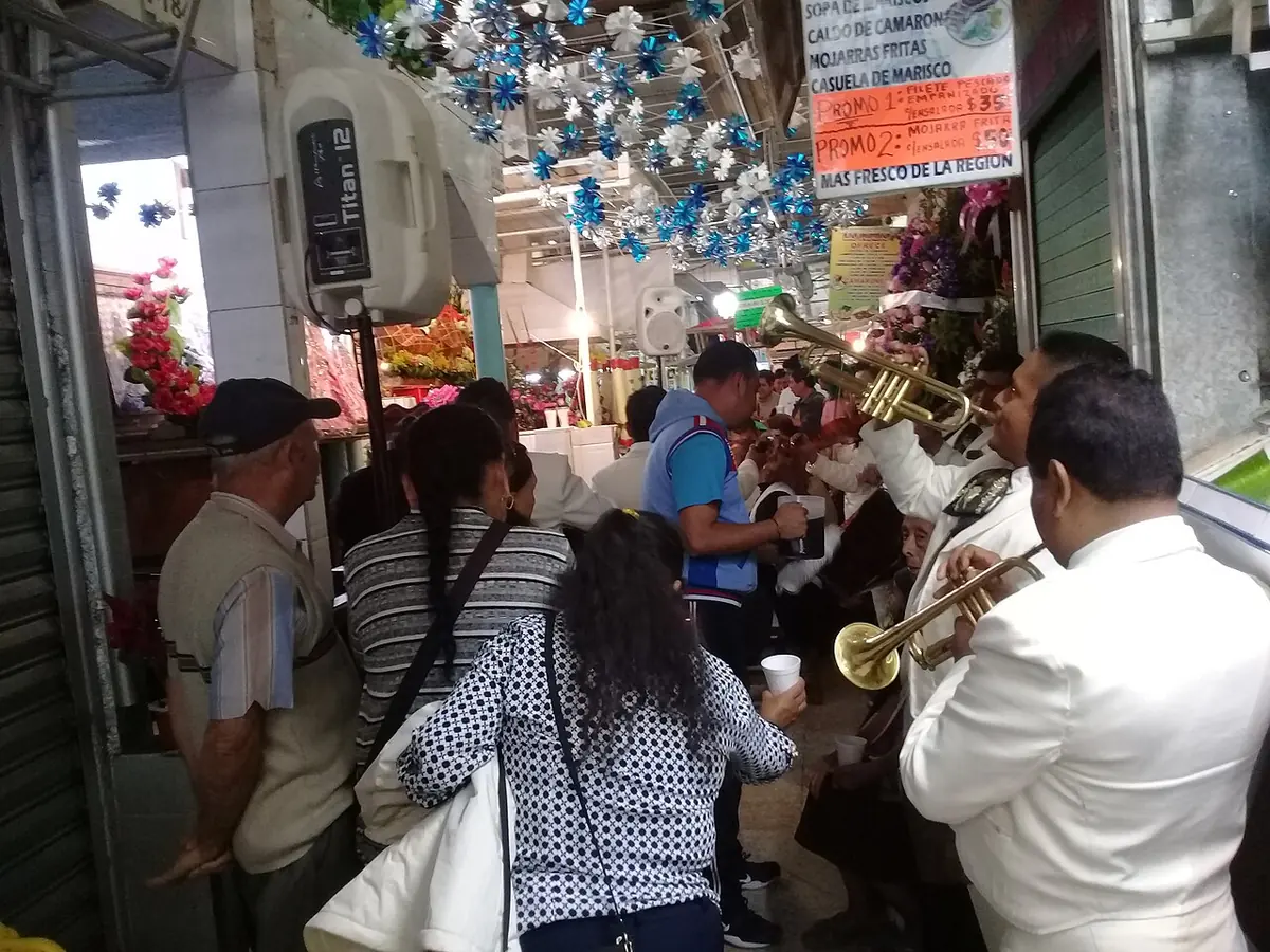 Mariachis con trompetas y fieles reunidos en un pasillo del mercado de Orizaba, adornado con papel picado, para cantarle las mañanitas a la Virgen de Juquila