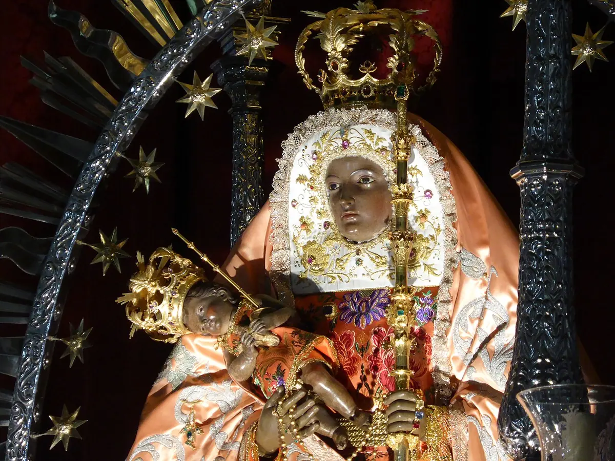 Primer plano de la imagen de la Virgen de Candelaria, de rostro moreno, con corona de oro y manto bordado, que sostiene al Niño Jesús coronado y un cirio dorado