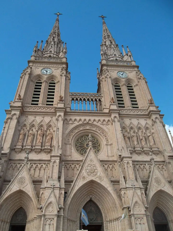 La fachada rosada de la basílica de Luján, con dos altas torres puntiagudas, un rosetón y tres portales, bajo un cielo azul