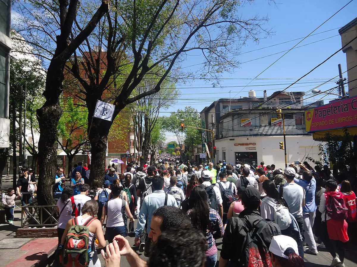 Una multitud de jóvenes con mochilas camina por una avenida arbolada durante la peregrinación juvenil a Luján, en un día de sol