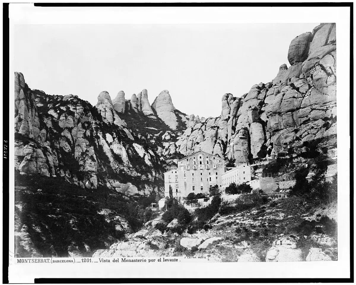 Fotografía antigua de los edificios del monasterio de Montserrat al pie de enormes paredes de roca redondeadas y verticales