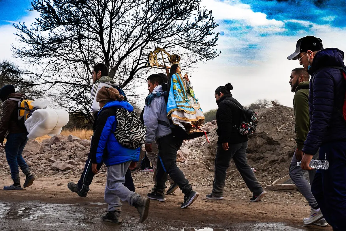 Un grupo de peregrinos con mochilas y chamarras camina por un camino de tierra; uno de ellos lleva a la espalda una imagen de la Virgen de San Juan