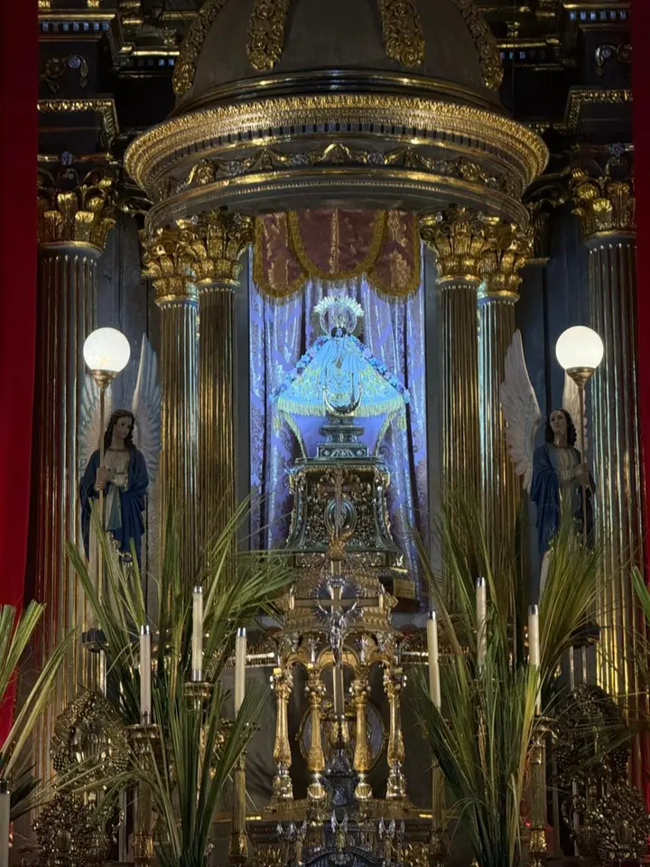 La pequeña imagen de la Virgen de Talpa con su manto azul y su corona, en su camarín dorado entre columnas, con lámparas y palmas a los lados
