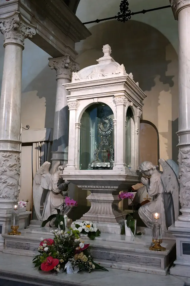 Altar de mármol blanco con estatuas de ángeles arrodillados a los lados y un alto tabernáculo de mármol con una custodia de plata, con flores al pie