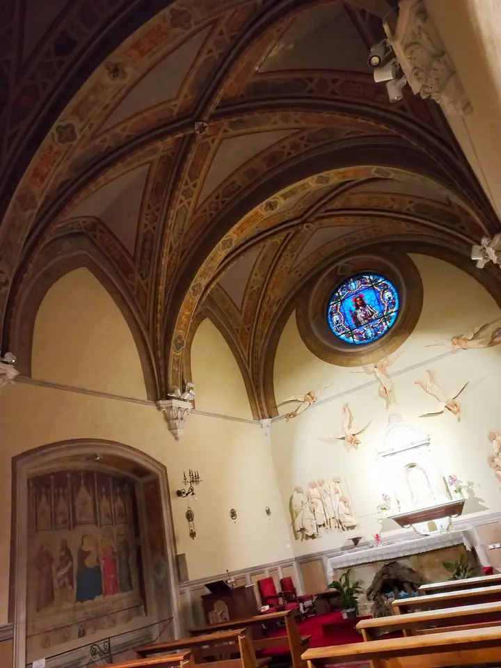 Capilla lateral abovedada con nervios pintados, un rosetón de vidrio de colores, un altar con ángeles esculpidos y filas de bancas
