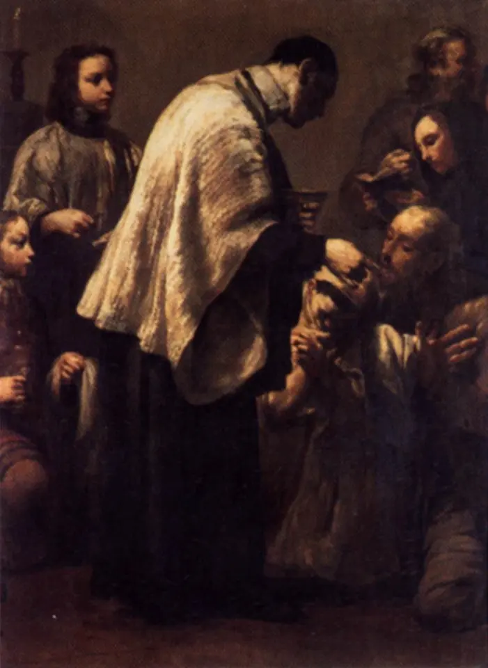 A priest in a white surplice, his back half turned to us, gives Holy Communion to kneeling men and boys in a dim church