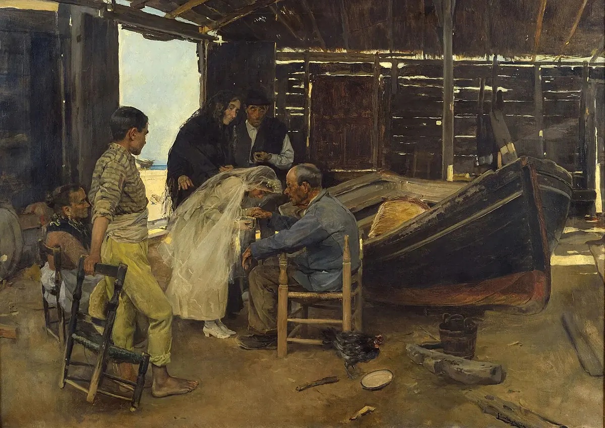 In a fishermen's boathouse in Valencia, a girl in a white dress and veil bends to greet her seated grandfather while family members gather around her beside a beached boat