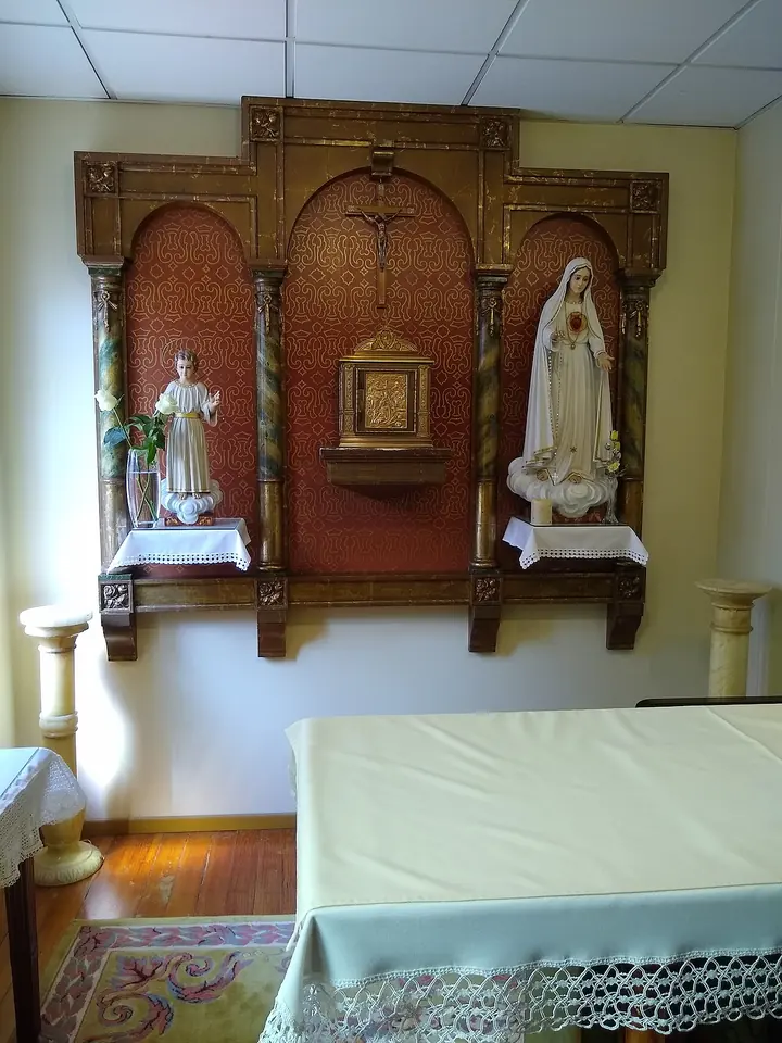 Small chapel with a carved wooden altarpiece holding statues of the Child Jesus and the Virgin Mary in white, a crucifix and a tabernacle above a white altar
