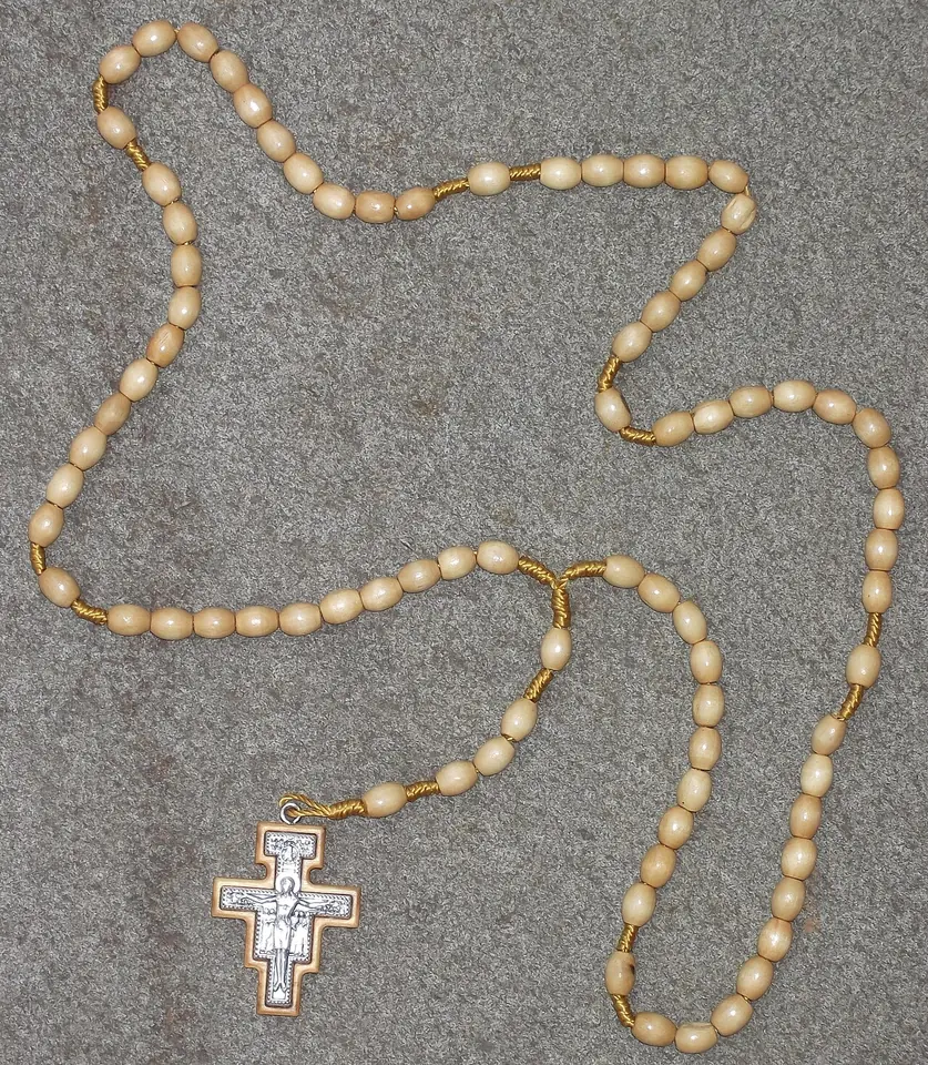Rosary of cream-colored oval beads on gold links, laid out on gray fabric and ending in a small San Damiano crucifix