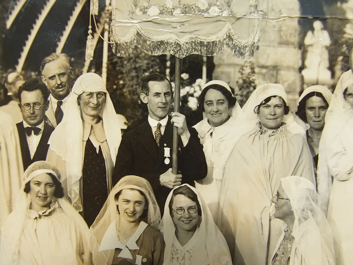 Old sepia group photograph of women in white veils and capes and a few men in suits gathered under a processional canopy, with Frank Duff in the center