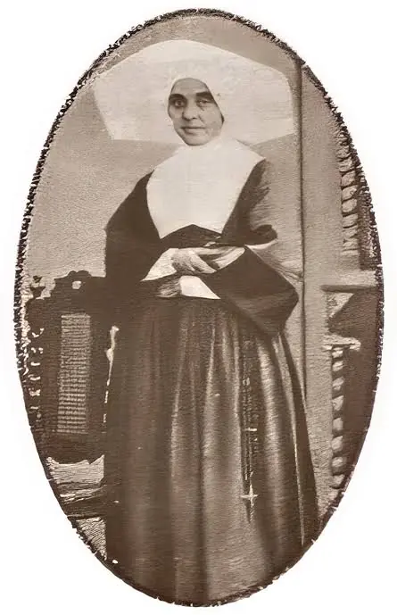 Old oval photograph of a Daughter of Charity standing in a dark habit and large white collar and headdress, her hands folded at her waist and a rosary at her side