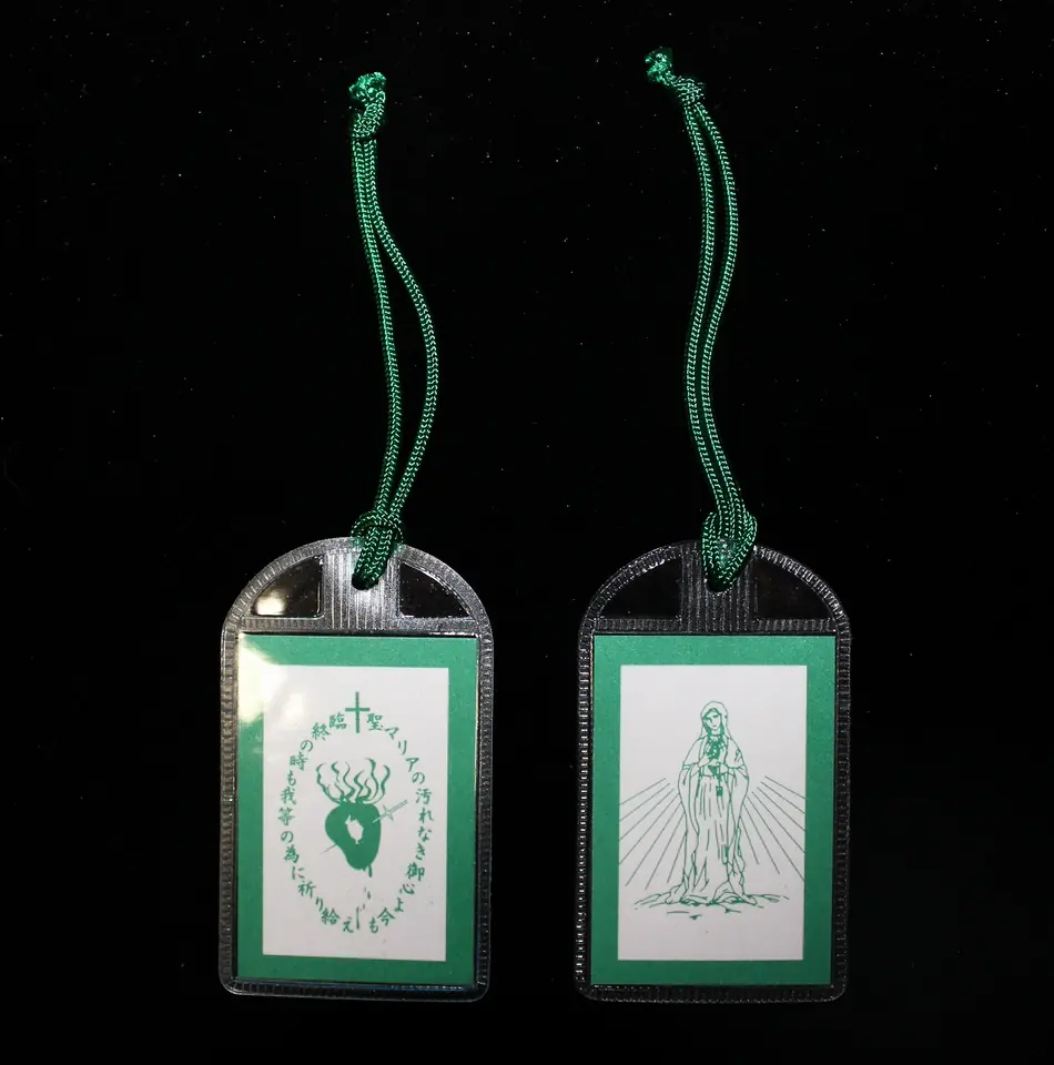 Both sides of a small laminated green scapular on a green cord, one showing the Virgin Mary with rays and the other a pierced, flaming heart inside an oval inscription under a cross