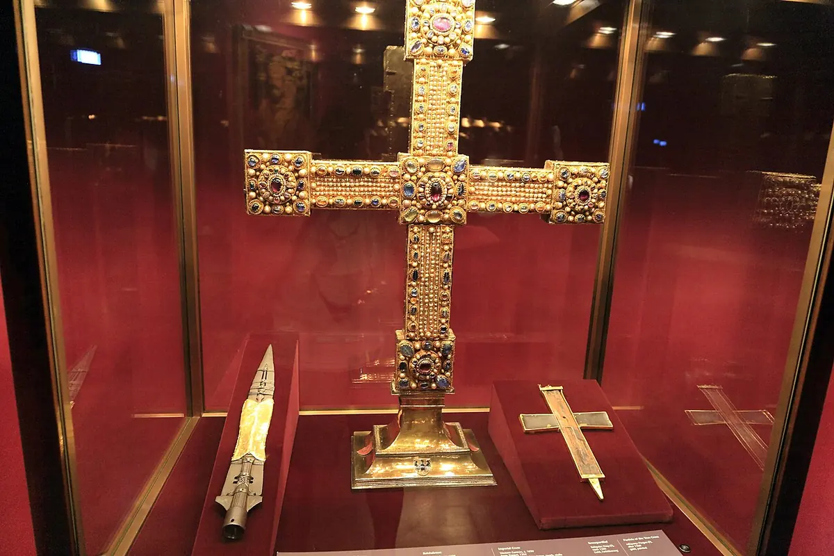 A glass case with a spearhead on the left, a large gold jeweled cross in the center and a small cross-shaped relic on red cloth on the right