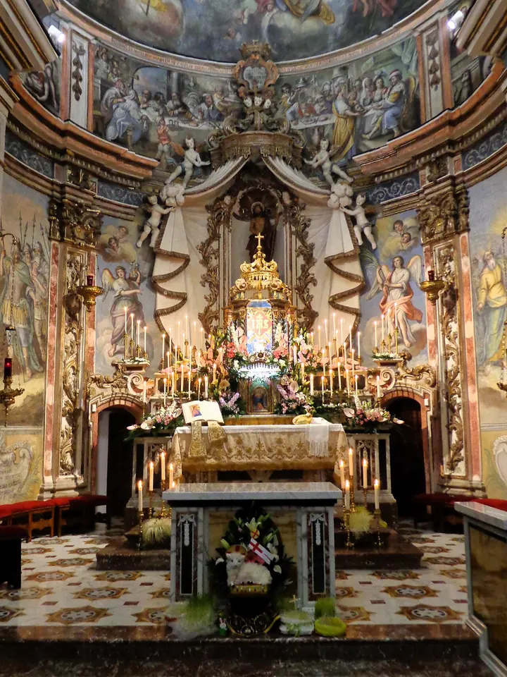 Presbiterio barroco de una iglesia de Sicilia en la noche del Jueves Santo, con un pequeño altar de la reserva cubierto de velas y flores blancas bajo un alto retablo dorado