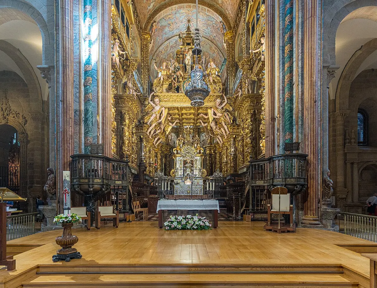 A gilded Baroque altarpiece with angels and a seated statue of St. James above an altar, under a large hanging censer, in a Romanesque cathedral