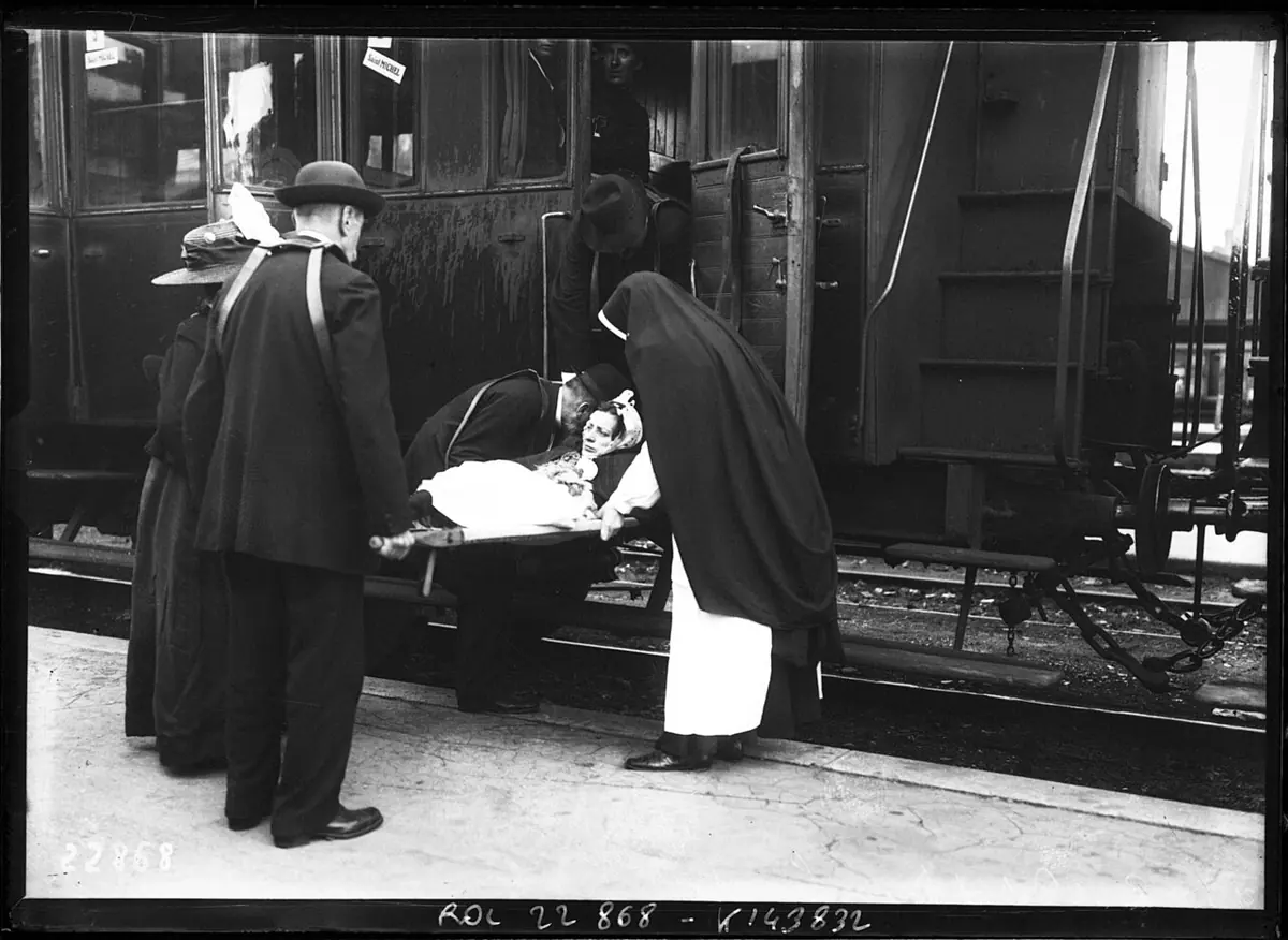 Press photograph of men and nuns lifting a woman on a stretcher into a railroad car at a Paris station